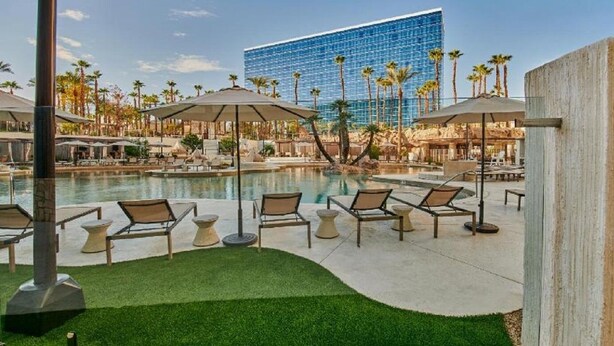 A pool area with lounge chairs and umbrellas, a water feature, and a modern building in the background. - Beautiful Hotel 2 mins from the strip-The Virgin Hotel- (Las Vegas)