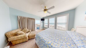 A bedroom with a bed, a chair, a ceiling fan, and a view of the beach through the windows. - Beachfront Paradise | Poolside Escape | Perfect Spring Break Vacation | Margartia Villas A (North Myrtle Beach)