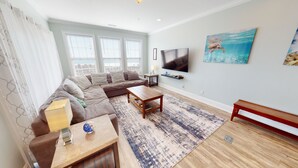 A modern living room with a sectional sofa, a coffee table, and a TV mounted on the wall. - Beachfront Paradise | Poolside Escape | Perfect Spring Break Vacation | Margartia Villas A (North Myrtle Beach)