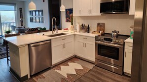 A modern kitchen with white cabinets, stainless steel appliances, and a large island with a sink. - Condo minutes from Broadway (Nashville)