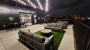 An outdoor seating area with sofas and tables, a bar area with stools, and a view of the cityscape at night. - Condo minutes from Broadway (Nashville)