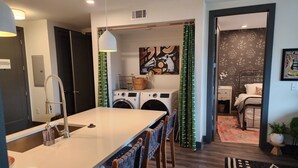 A modern kitchen with a central island, a washing machine, and a dining area with bar stools. - Condo minutes from Broadway (Nashville)