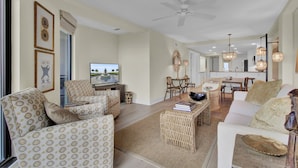 Un salon spacieux comprenant un canapé, des fauteuils, une table basse et un téléviseur. On aperçoit à l’arrière-plan un coin repas avec une table et des chaises.
