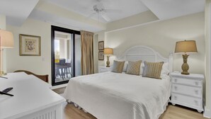 Une chambre avec un grand lit, deux tables de chevet avec des lampes, un ventilateur de plafond et une vue sur l’extérieur grâce à une porte vitrée.