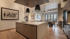 Een moderne keuken met een centraal eiland, hanglampen en een groot raam met uitzicht op een stadsbeeld.