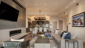 Een moderne woonkamer met een flatscreen televisie, een open haard, een eethoek en een keuken op de achtergrond.