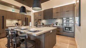Een moderne keuken met een centraal eiland, barkrukken en roestvrijstalen apparatuur.