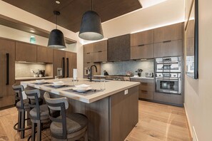 Una cocina moderna con una isla central, taburetes de bar y electrodomésticos de acero inoxidable.