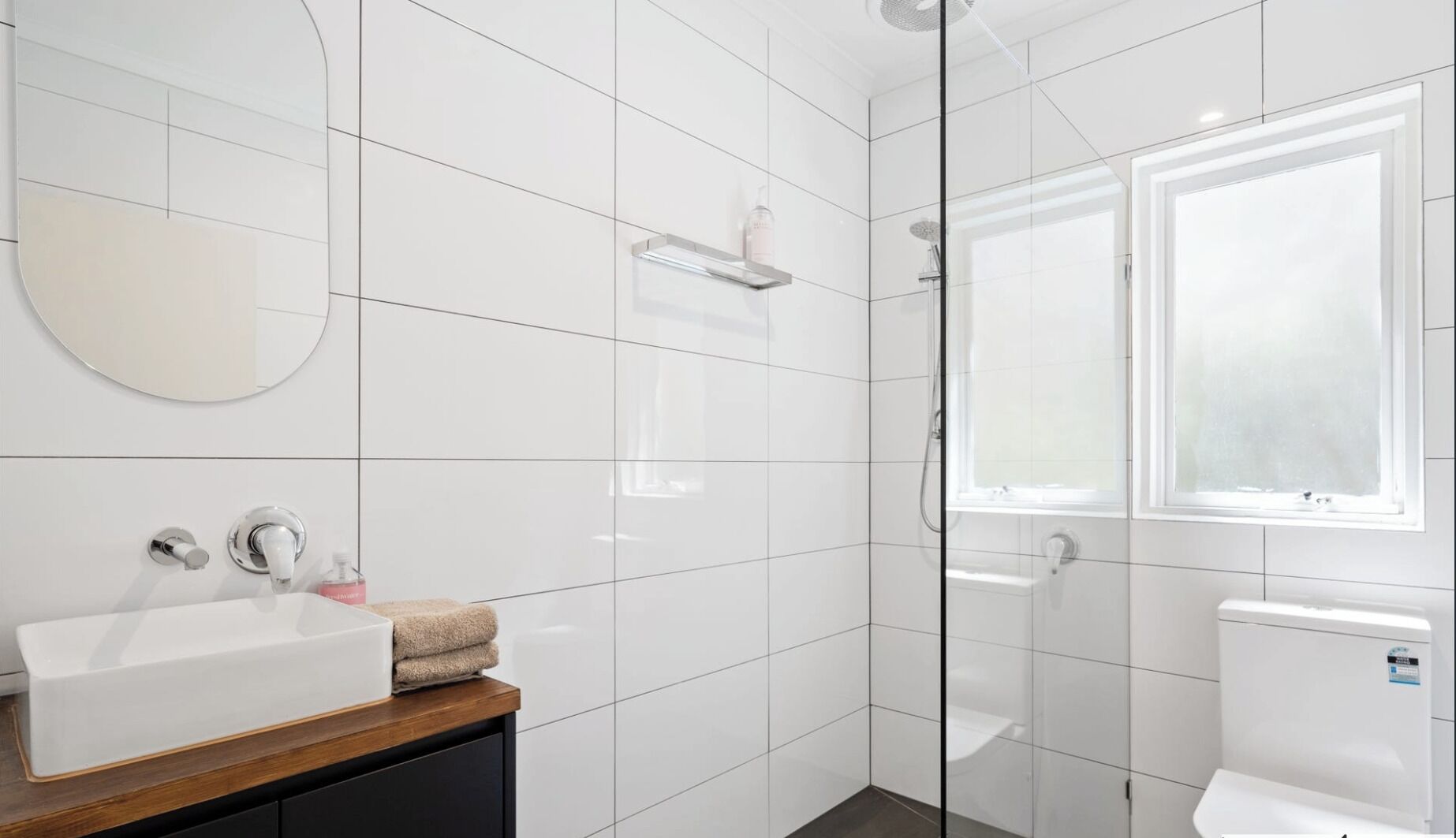 Une salle de bain moderne avec un lavabo blanc, un miroir et un espace douche.