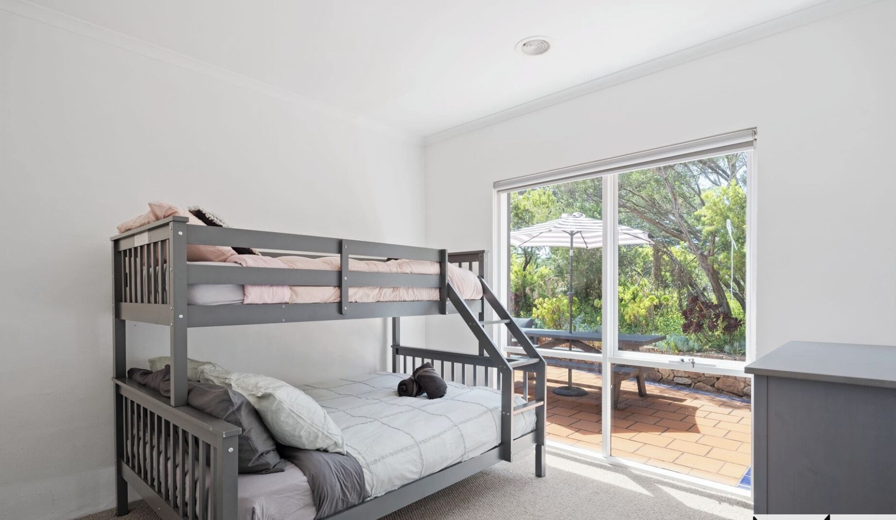 A bunk bed room with a view of the garden through large windows.