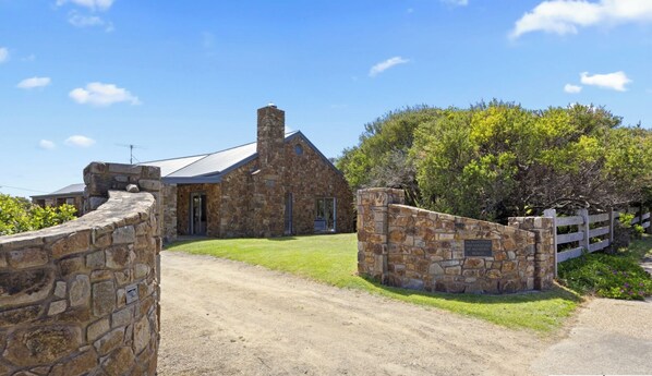 A stone building with a metal roof, a paved driveway, and a wooden fence.