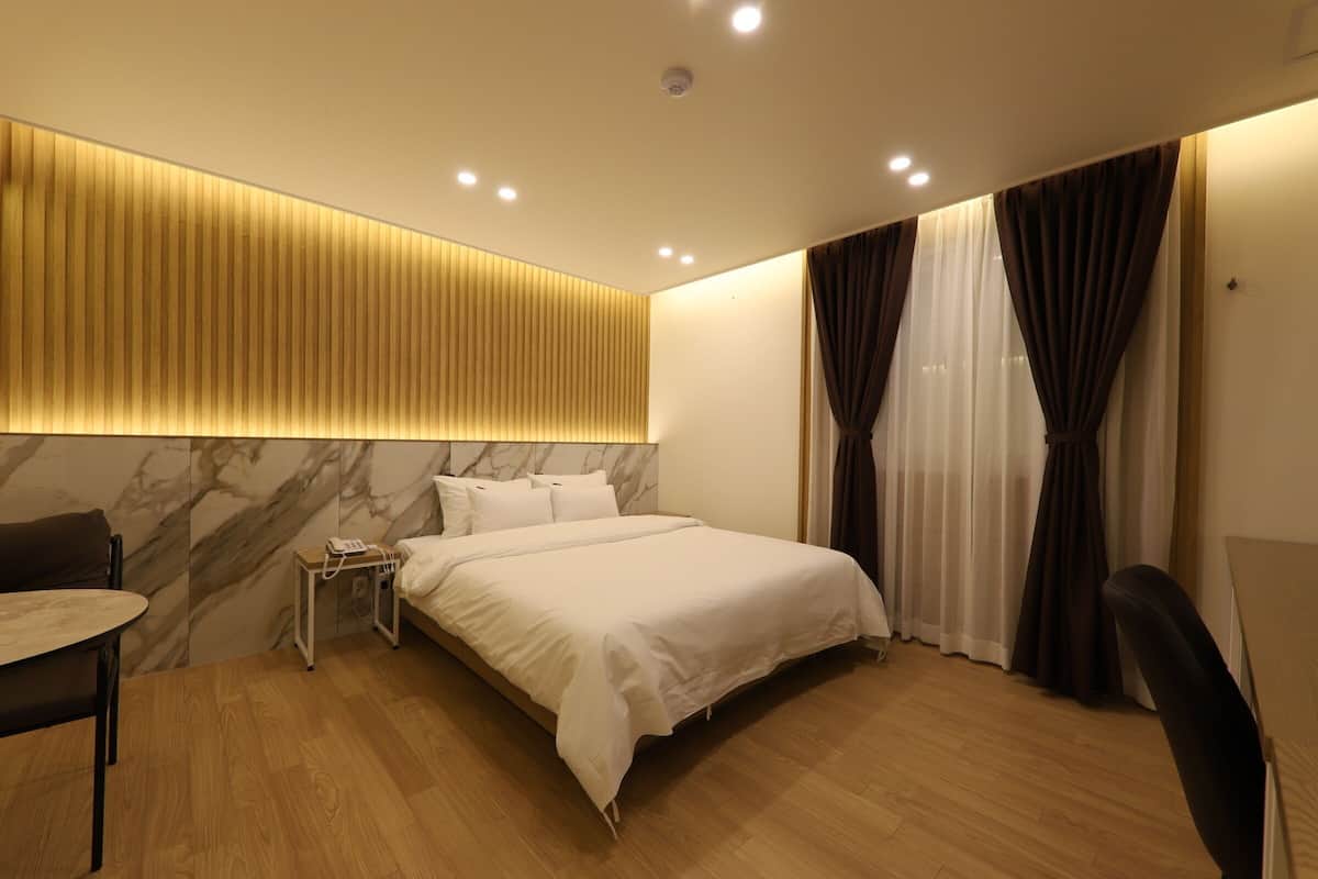 Ein modernes Hotelzimmer mit Bett, Nachttisch und Schreibtisch mit Stuhl.