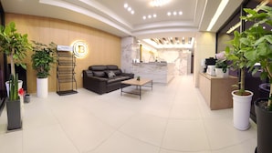 Een moderne lobby met een receptiebalie, een bank en potplanten.