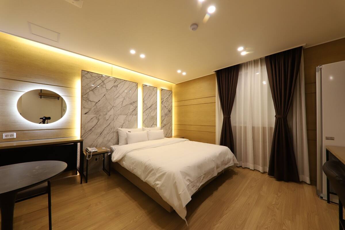 Ein modernes Hotelzimmer mit Bett, Nachttisch, Schreibtisch und einem großen Spiegel.