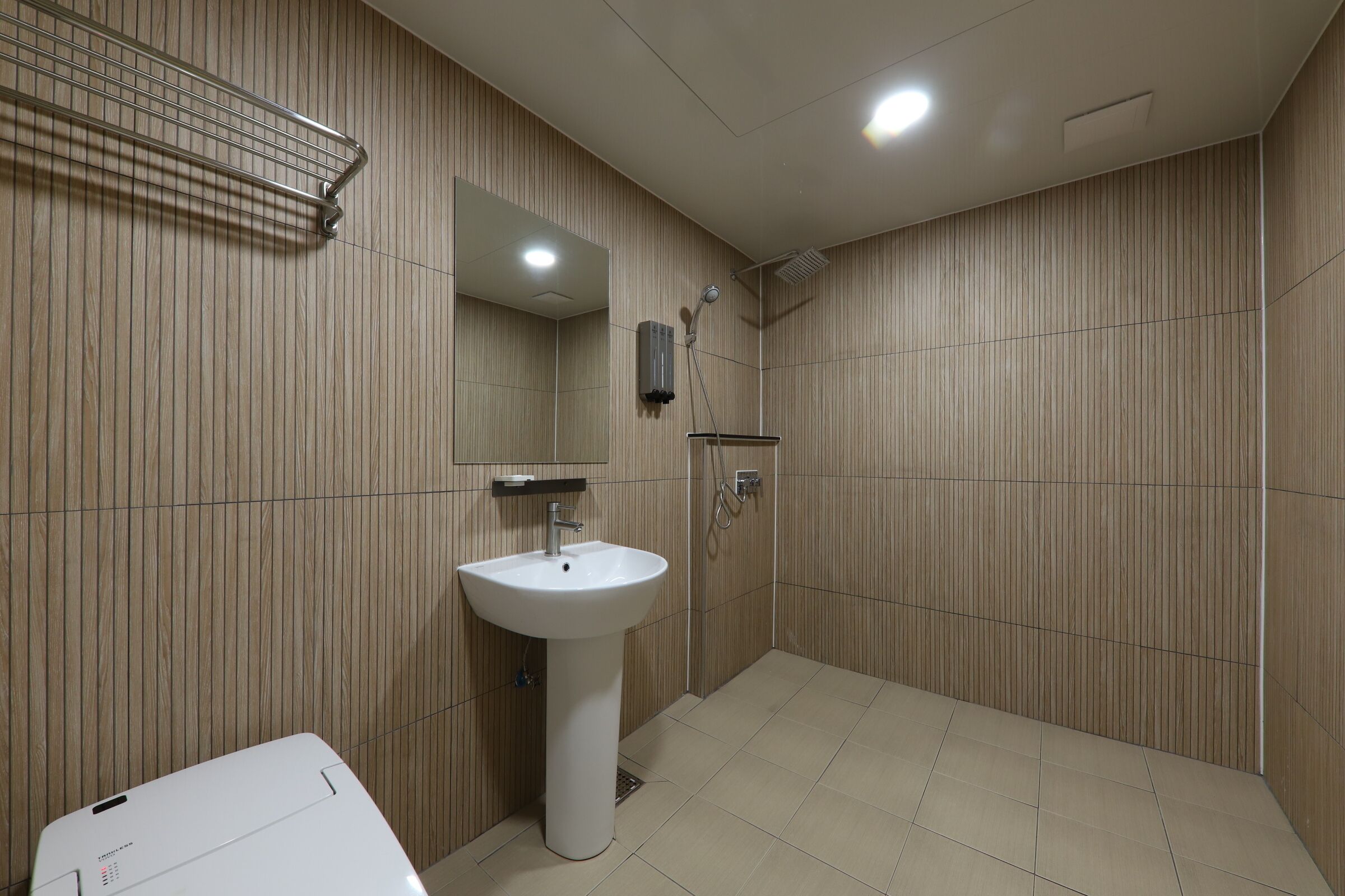 A modern bathroom with a pedestal sink, a mirror, a shower, and a towel rack.