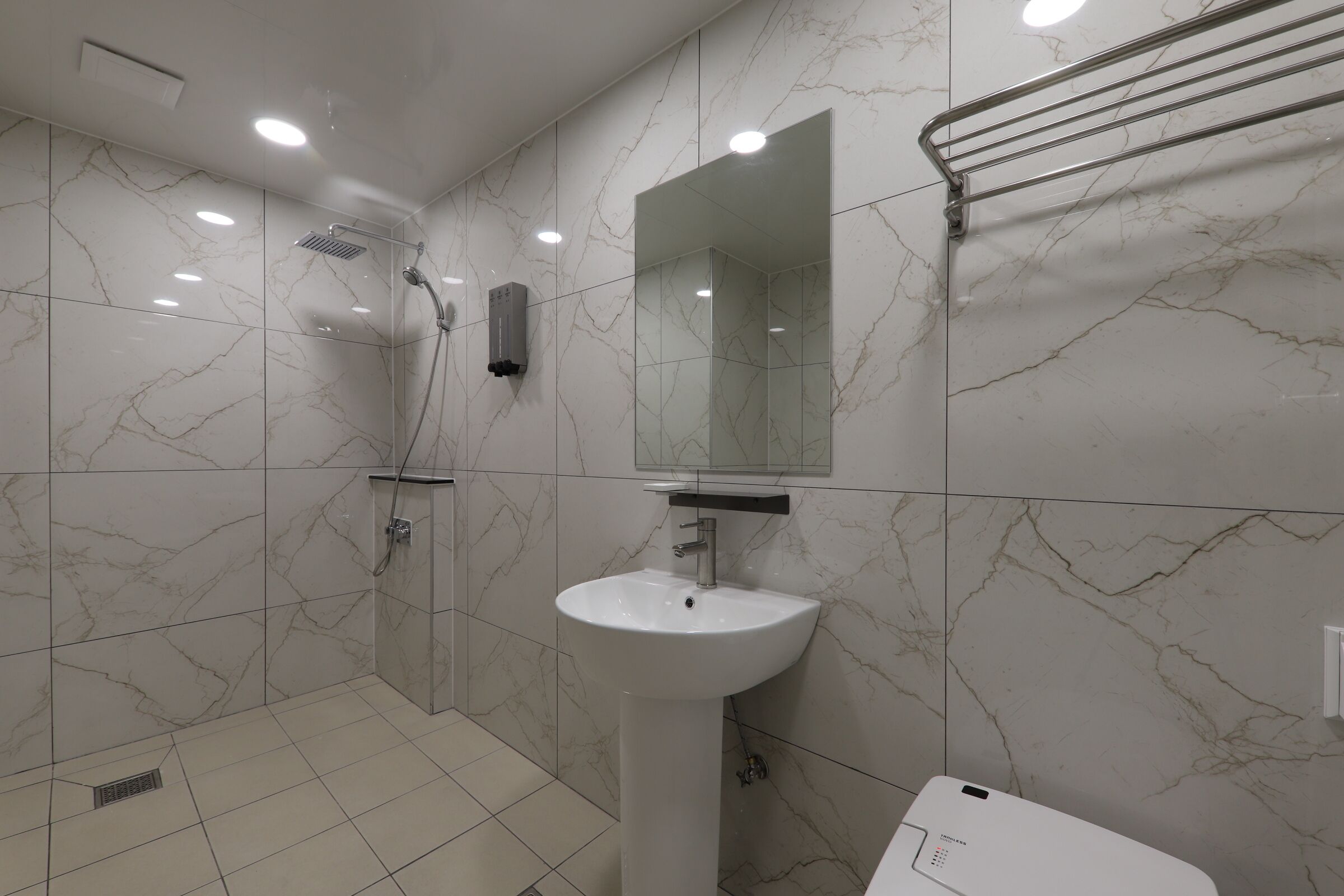 A modern bathroom with a white sink, a glass shower enclosure, and a marble-tiled wall.