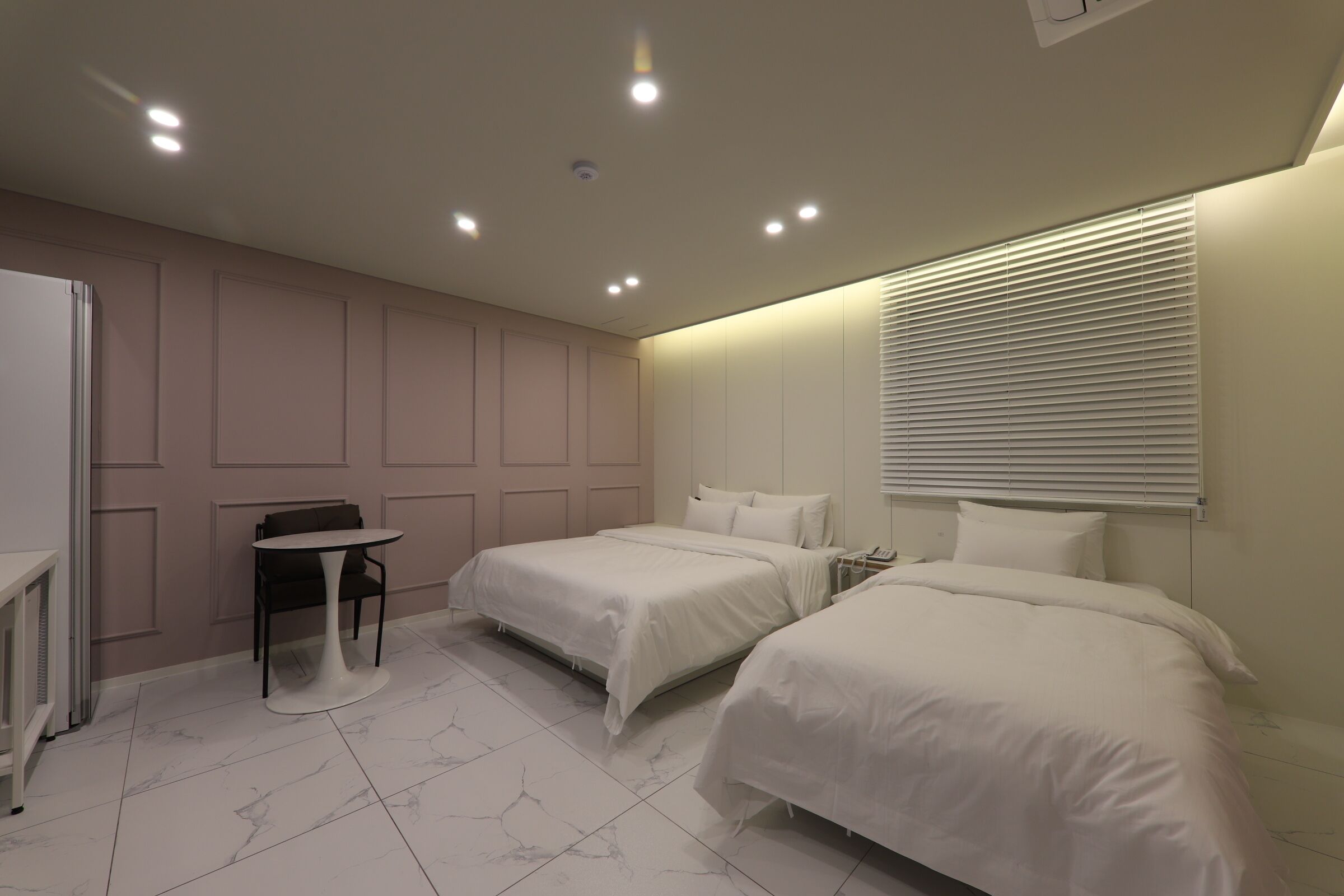 Quarto de hotel com duas camas, uma mesa pequena e uma cadeira.