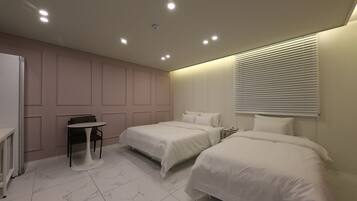 Quarto de hotel com duas camas, uma mesa pequena e uma cadeira.