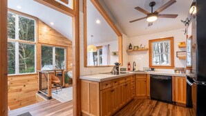 Une cuisine moderne avec des meubles en bois, un lave-vaisselle noir et une grande fenêtre donnant sur un paysage enneigé.