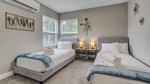 Een slaapkamer met twee bedden, een klein tafeltje met lampen en decoratieve wandkunst.