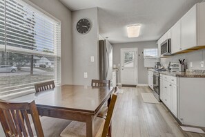 A modern kitchen with white cabinets, a wooden dining table, and a clock on the wall.