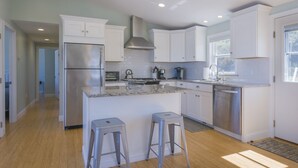 A modern kitchen with white cabinets, stainless steel appliances, and a granite countertop. - Oceanfront Property with AC in Scorton Shores (East Sandwich)