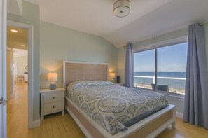 A bedroom with a large bed, a nightstand, a lamp, and a view of the sea.