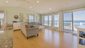 A spacious living room with a large window overlooking the ocean, a ceiling fan, and a wooden floor. - Oceanfront Property with AC in Scorton Shores (East Sandwich)