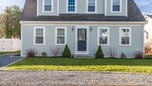 A two-story house with a front porch, a garage, and a well-maintained lawn. - Cape Cod Home—Deck, Near Canal & Bike Path (Sandwich)
