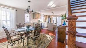 A spacious kitchen with wooden cabinets, a dining area with a glass table, and a staircase. - Cape Cod Home—Deck, Near Canal & Bike Path (Sandwich)