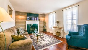 A living room with a fireplace, a sofa, a blue armchair, and a coffee table. - Cape Cod Home—Deck, Near Canal & Bike Path (Sandwich)
