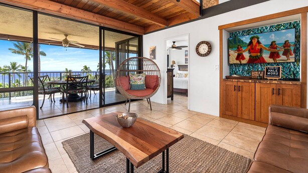 A spacious living area with a wooden ceiling, a large window overlooking the ocean, a dining table, and a cozy seating area.