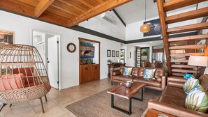 A spacious living room with a high ceiling, a wooden staircase, and a dining area.