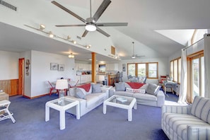 A spacious living room with a ceiling fan, a dining area, and a kitchen in the background.