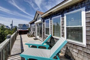 A wooden deck with a lounge chair and a table, overlooking a residential area with houses.