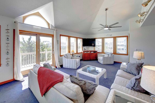 A spacious living room with a large window, a ceiling fan, and a television.