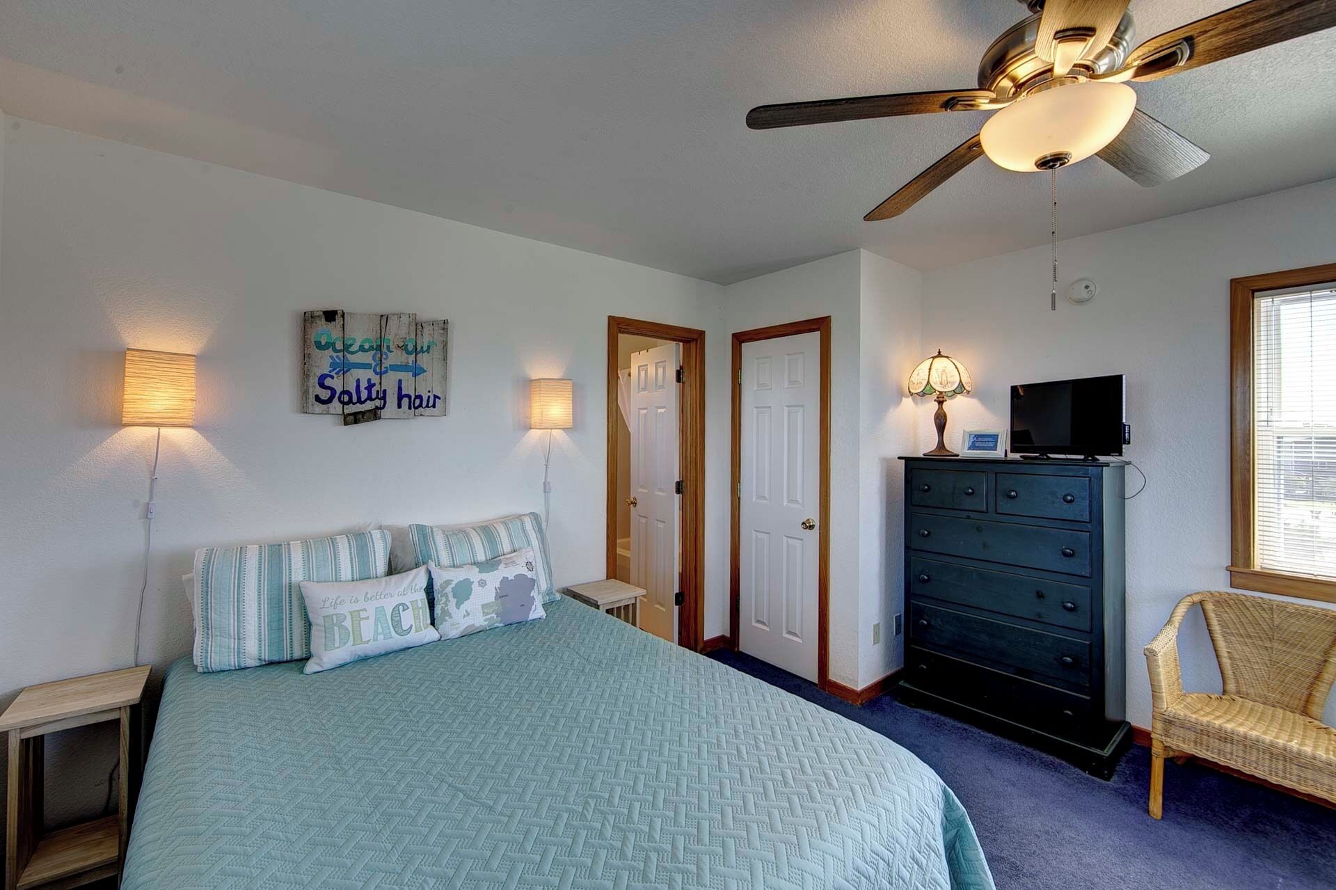 Une chambre à coucher comprenant un lit, une commode, une chaise, un ventilateur de plafond et deux portes.