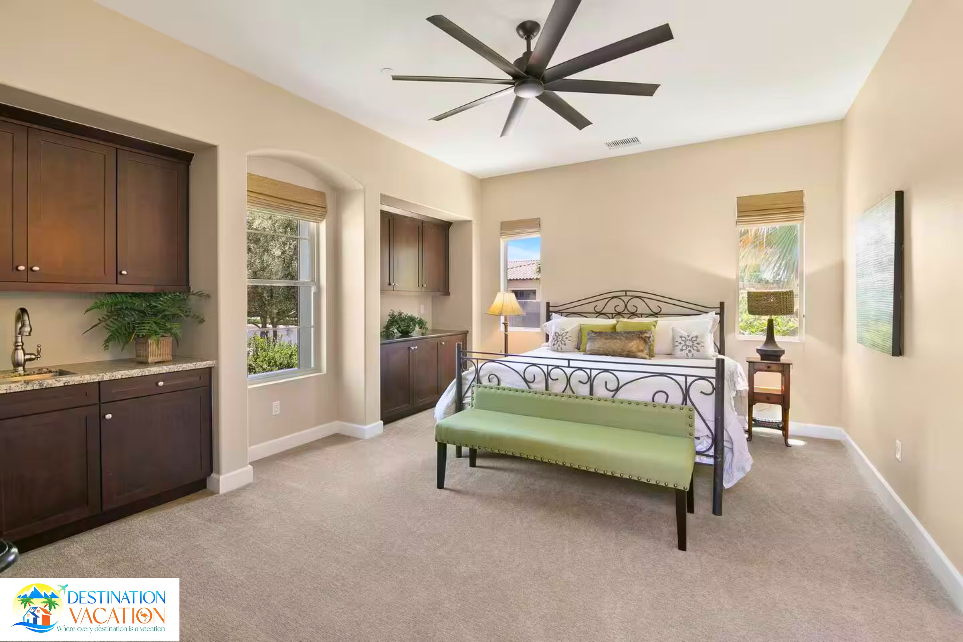 A bedroom with a bed, a bench, a ceiling fan, and a view of the outdoors.