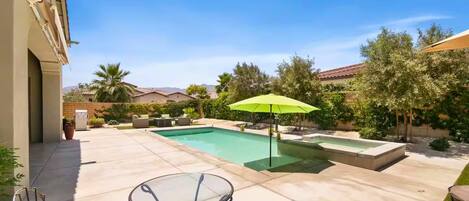 A backyard with a swimming pool, a table with chairs, and a green umbrella.
