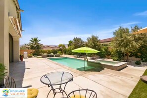 Un patio trasero con piscina, una mesa de vidrio y un paraguas verde.