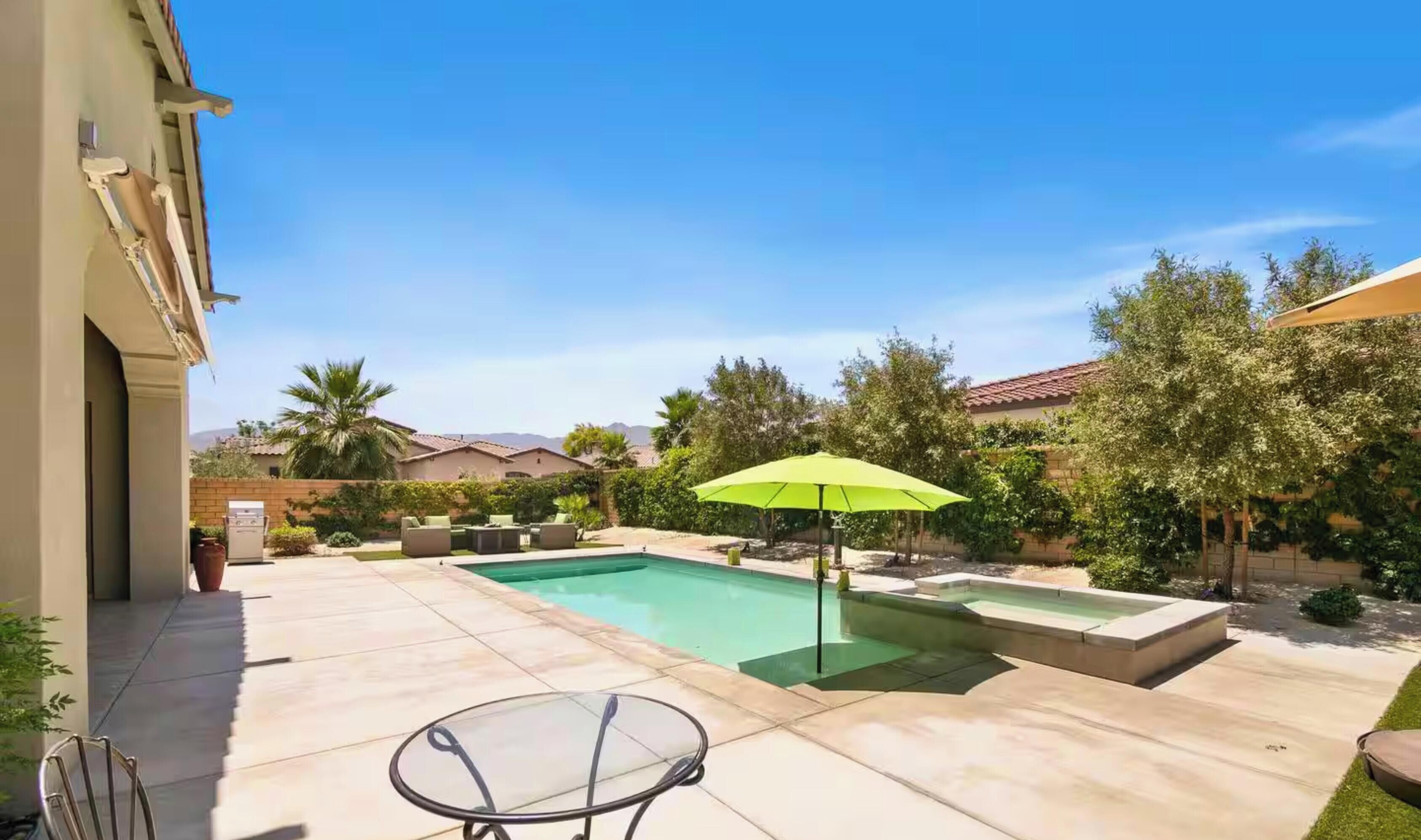 A backyard with a swimming pool, a glass table, and a green umbrella.