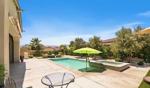 Un jardin avec une piscine, une table en verre et un parasol vert.