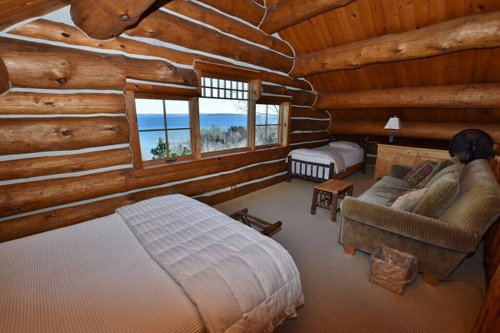 Une chambre située dans un chalet en rondins, avec un lit, un canapé, une petite table et une fenêtre donnant sur le paysage extérieur.