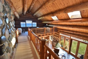 A log cabin with a stone wall, wooden deck, and large windows. - Luxury Waterfront Log Home 15 min from Traverse City w/ Dock (Suttons Bay)