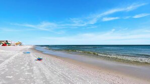 Une plage avec un ciel dégagé, quelques personnes et une petite voiture jouet sur le sable.