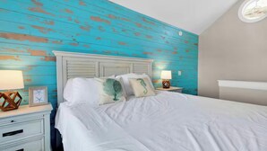 Une chambre à coucher avec un lit, deux tables de chevet et un mur dont la peinture turquoise est vieillie.