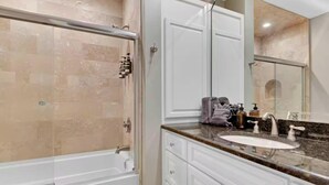 Une salle de bain dotée d’une douche à parois de verre, d’un lavabo blanc avec un plan de toilette en marbre et d’un grand miroir.
