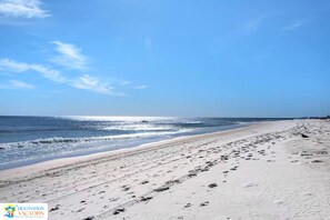 Una playa con cielo despejado, mar tranquilo y huellas en la arena.
