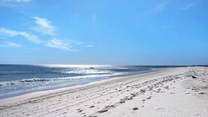 Ein Strand mit blauem Himmel, sandigem Ufer und Fußspuren, die ins Wasser führen.