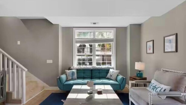 Un salon avec un canapé de couleur turquoise, un fauteuil blanc, une table basse et une fenêtre donnant sur des arbres.